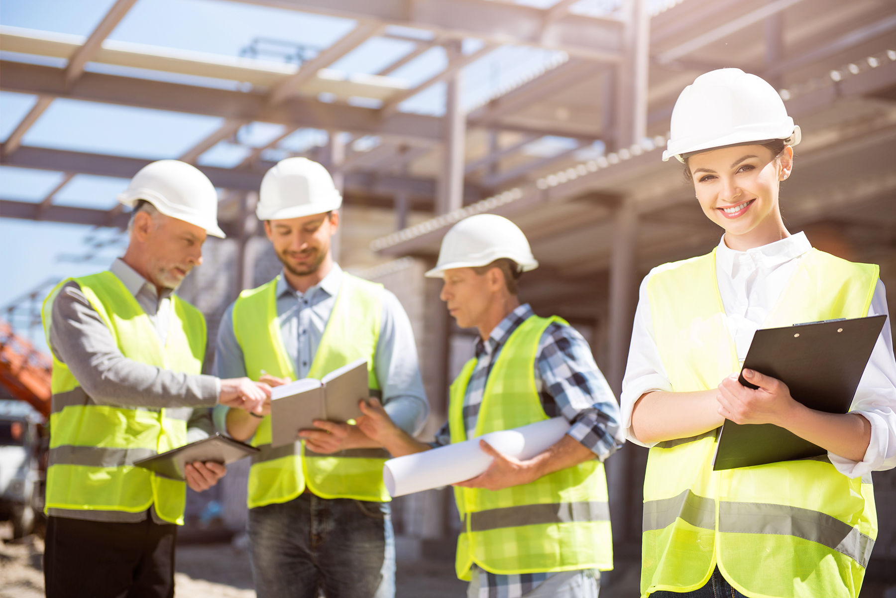 Construction site. A smiling and positive female engineer standing with papers with a group of engineers in a background